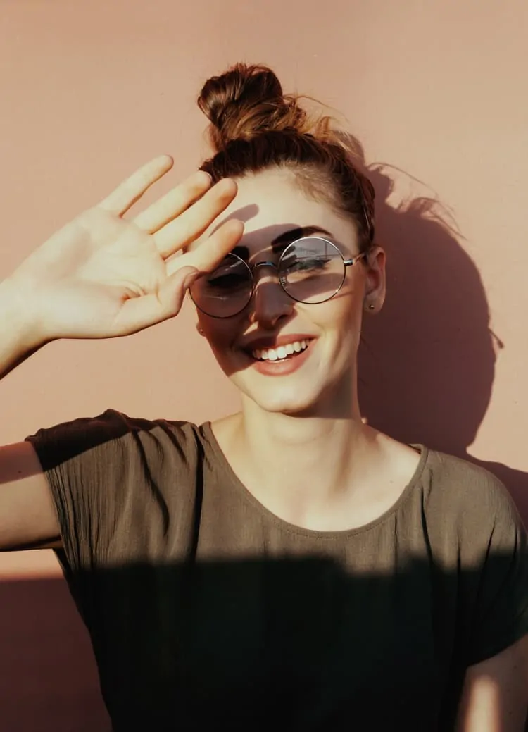 Frau mit Brille ohne Sonnenschutz-Gläser und UV-Filter wird von der Sonne geblendet